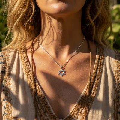 The silver Star of David pendant worn at the collarbone on a fine silver chain in warm sunlight