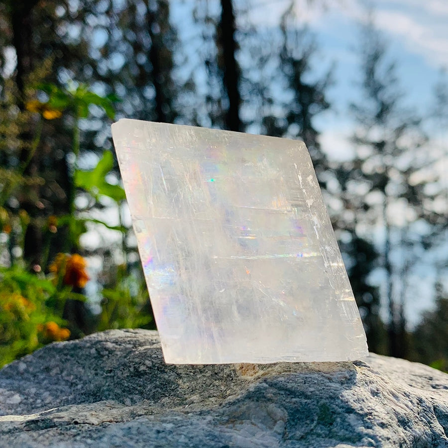 An optical calcite chunk standing on a rock in sunlight, with small rainbows glowing inside it