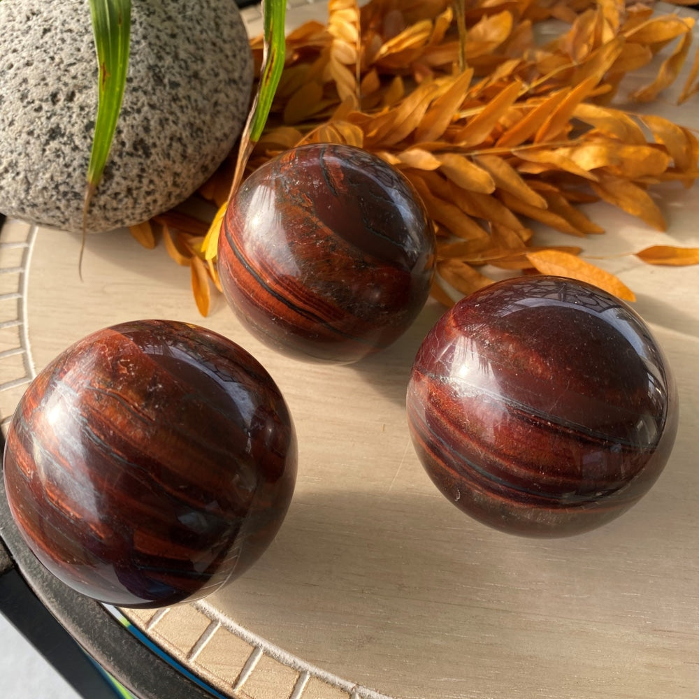 Three polished red tiger’s eye spheres on a wooden tray, each with its own red and dark brown banding
