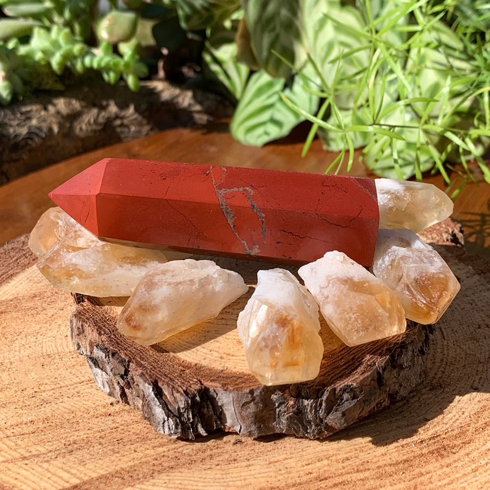 A polished red jasper point lying across seven raw citrine shards on a wooden slice