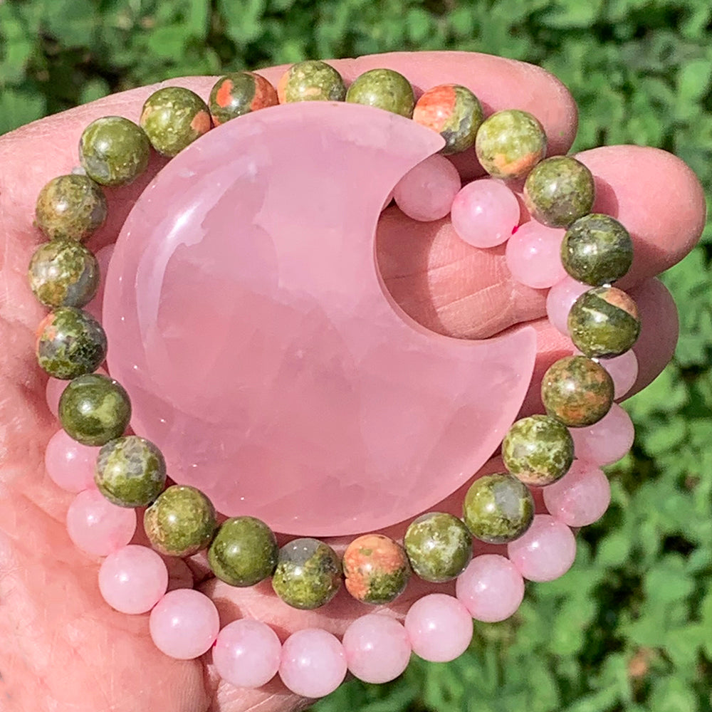 The pink rose quartz crescent moon resting in an open palm, circled by the rose quartz and unakite mala bracelets