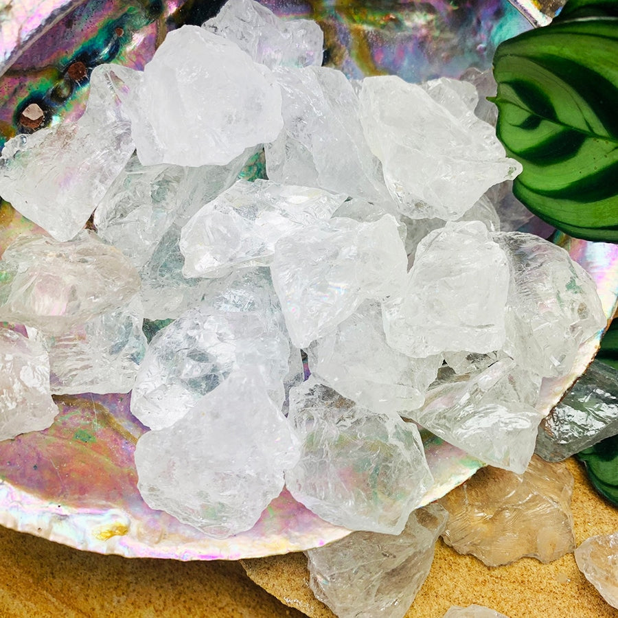 A pile of rough, glassy clear quartz pieces in an iridescent abalone shell