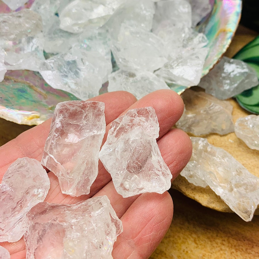 Several rough clear quartz pieces resting on the fingers of an open hand beside a shell of more pieces