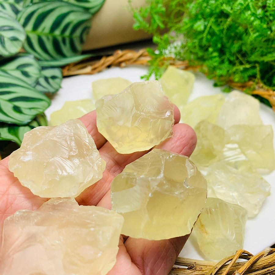 Rough pale-yellow lemon citrine pieces resting in an open palm above a dish of more