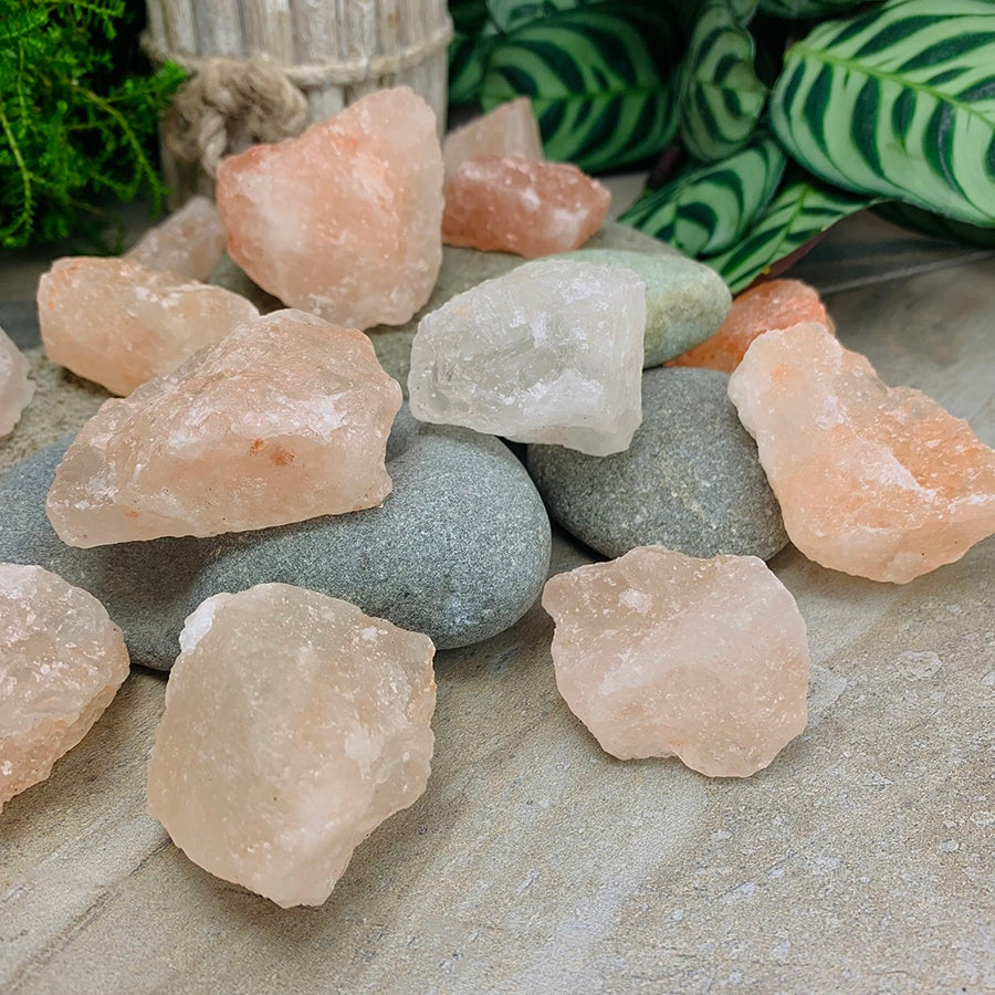 A selection of rough salt stones in blush pink and clear white, resting on smooth grey river stones