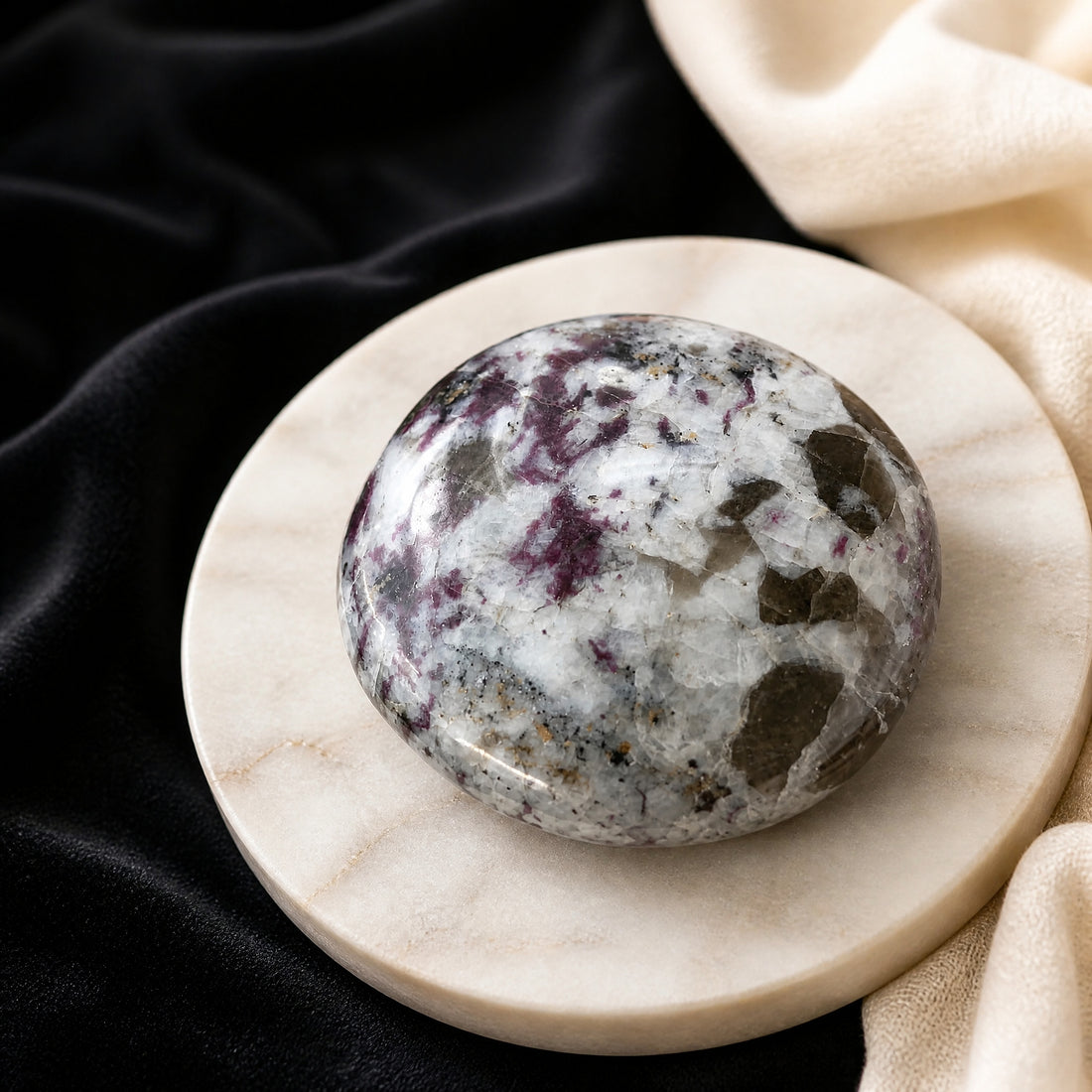 Polished rubellite tourmaline palmstone with raspberry-pink flecks on a pale marble dish