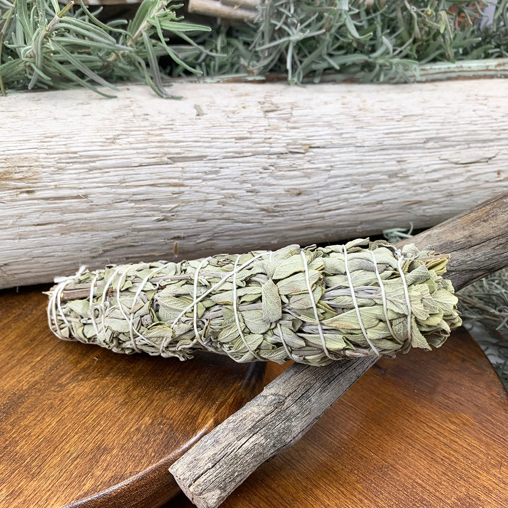 One dried sage bundle wrapped in white cotton string, resting on a wooden dish