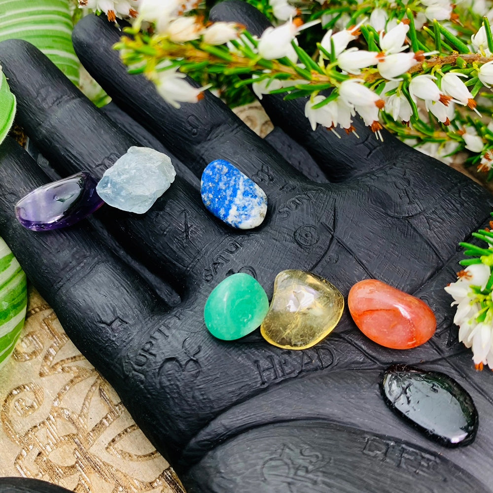 Seven mini gemstones, amethyst, celestite, lapis lazuli, aventurine, citrine, carnelian and tourmaline, resting on a carved palmistry hand