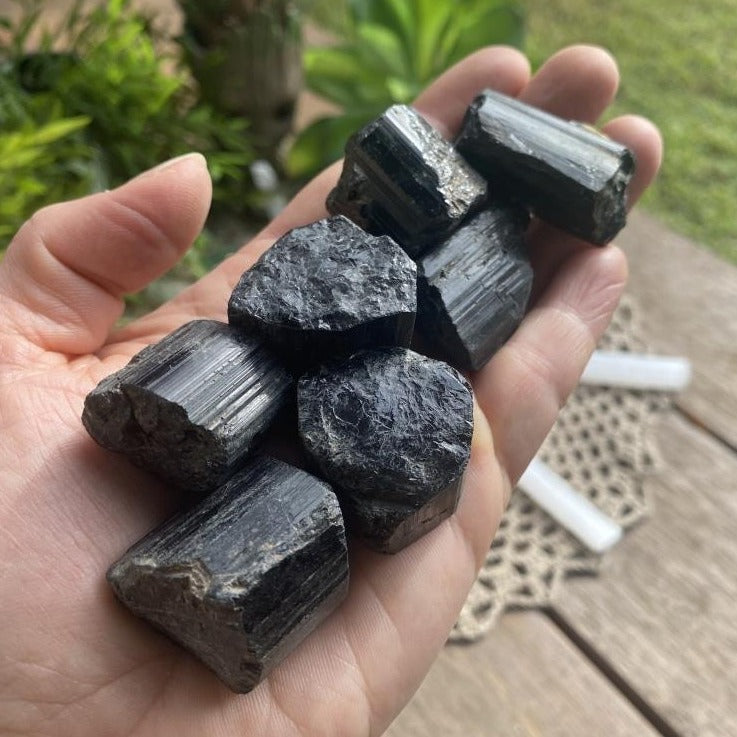 A handful of small rough black tourmaline chunks in different shapes resting in an open palm