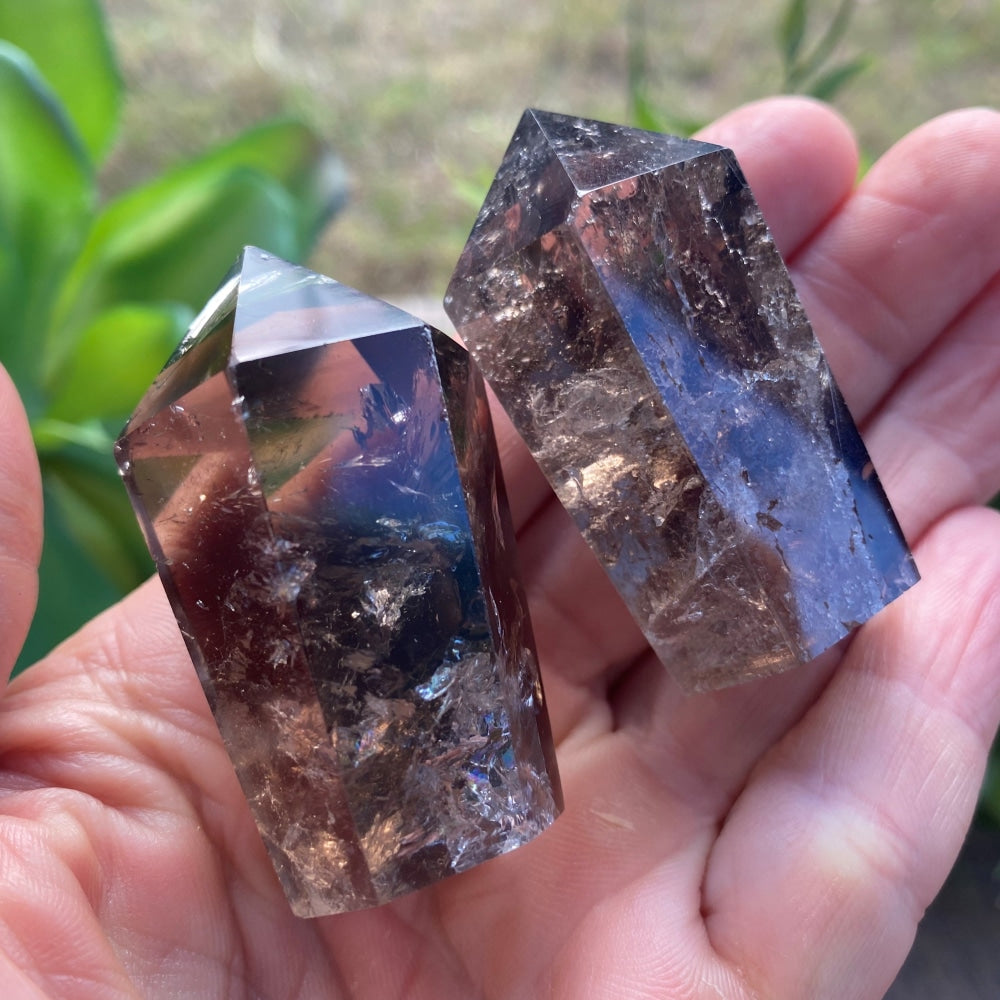 Two smoky quartz wands, one lighter and one darker, resting in an open palm