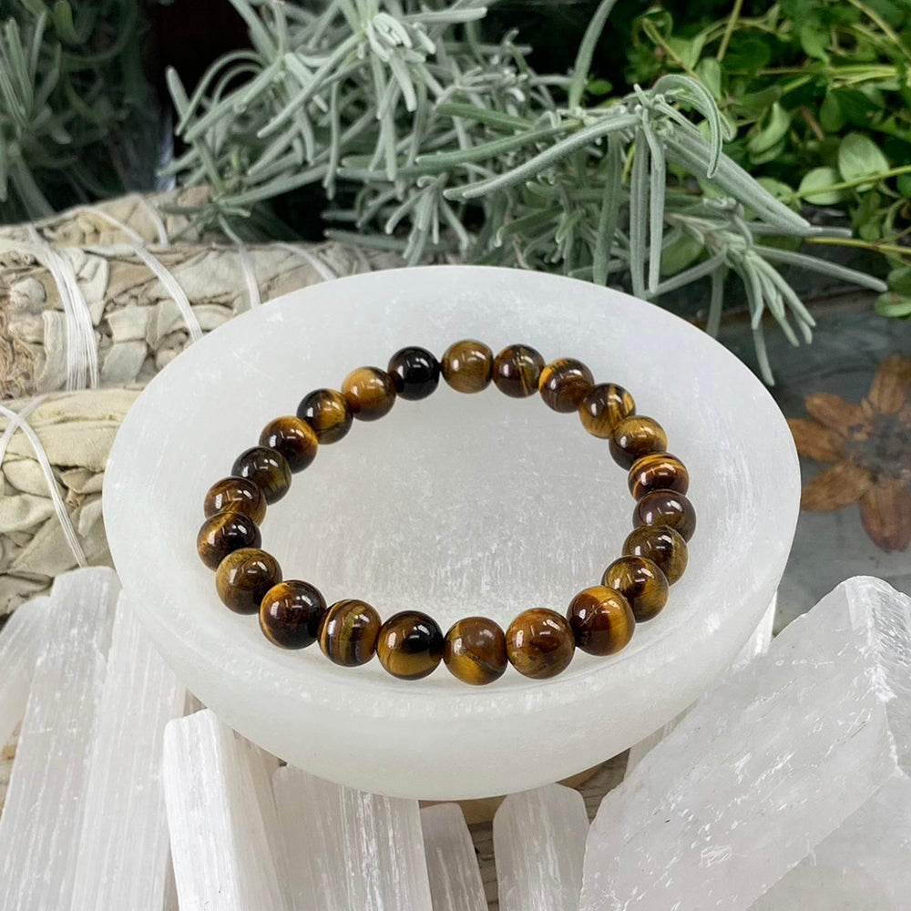 A tiger’s eye mala bracelet of round golden-brown banded beads resting in a white selenite bowl
