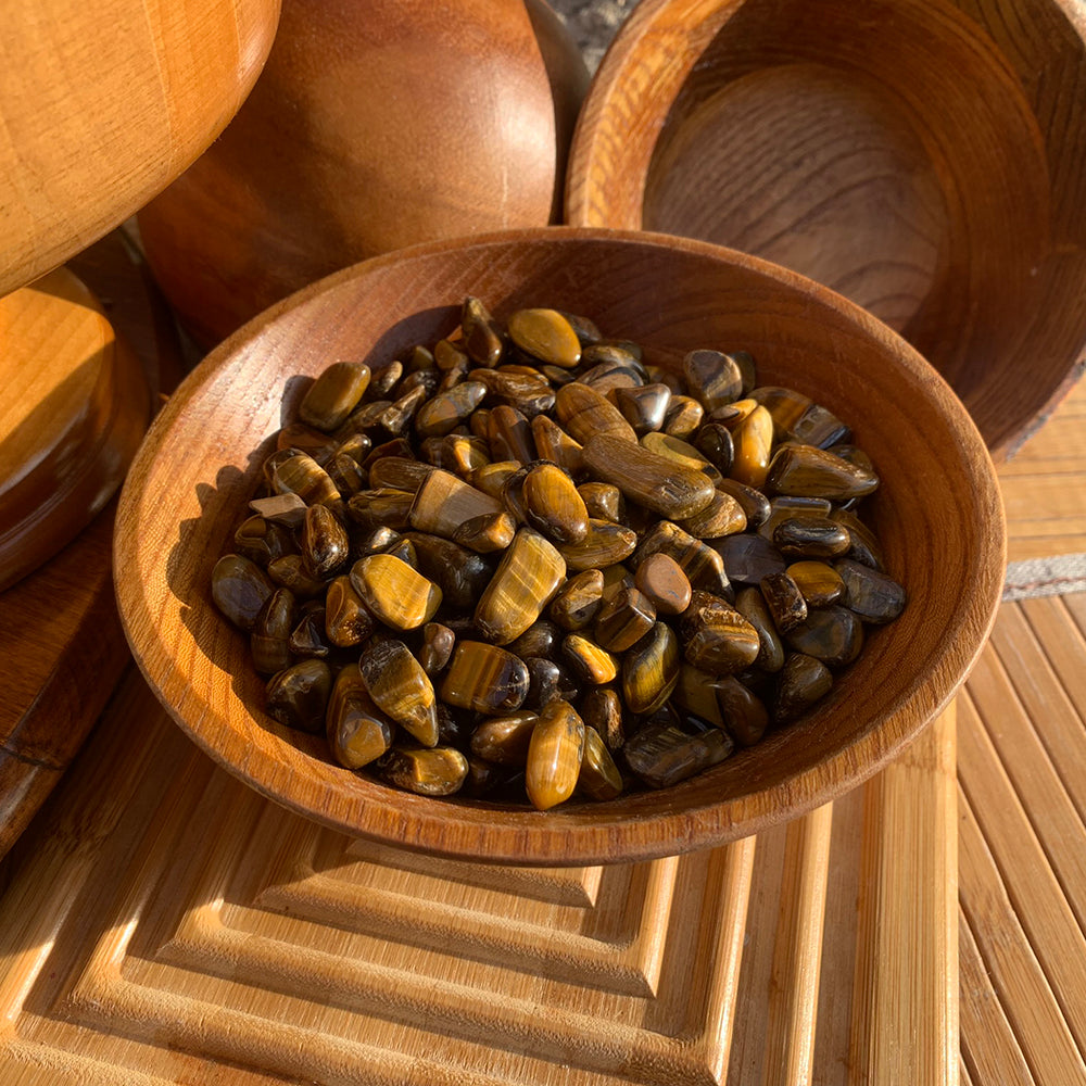 A wooden bowl filled with tiger’s eye mini gemstones on a bamboo board in warm sunlight