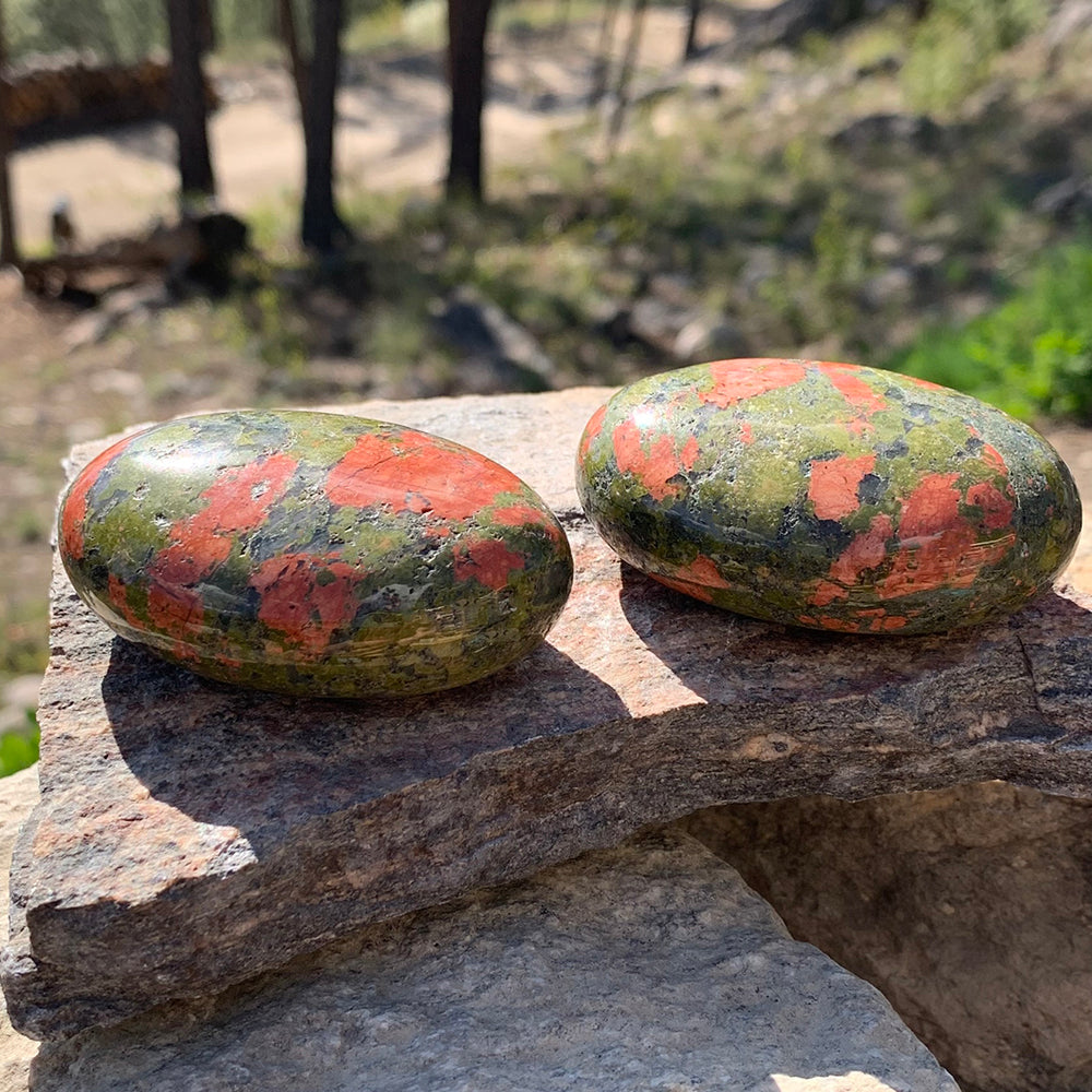 Two unakite palmstones on a sunlit granite ledge, each with its own scatter of pink patches across green