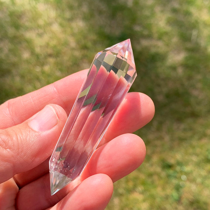 A 12-sided Vogel quartz wand resting across the fingers of an open hand outdoors