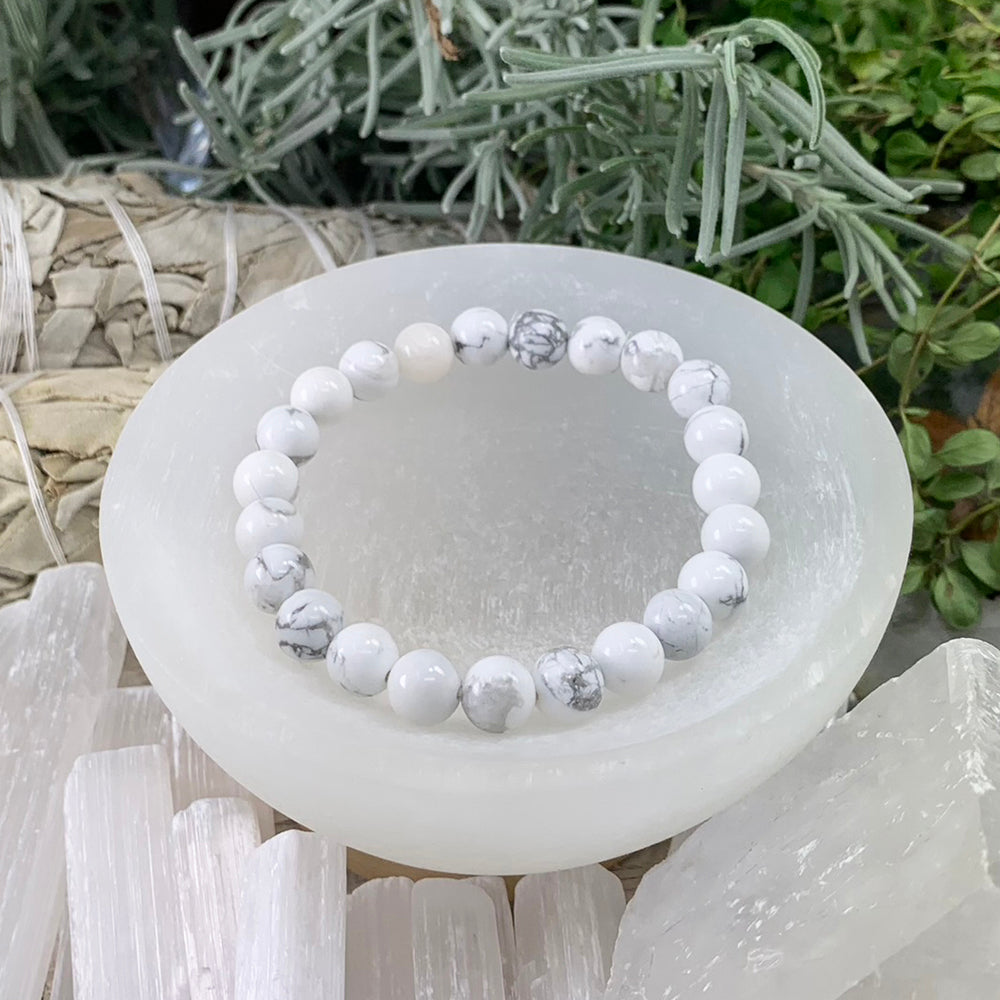 White howlite mala bracelet of round 8 mm beads with soft gray veins resting in a selenite bowl