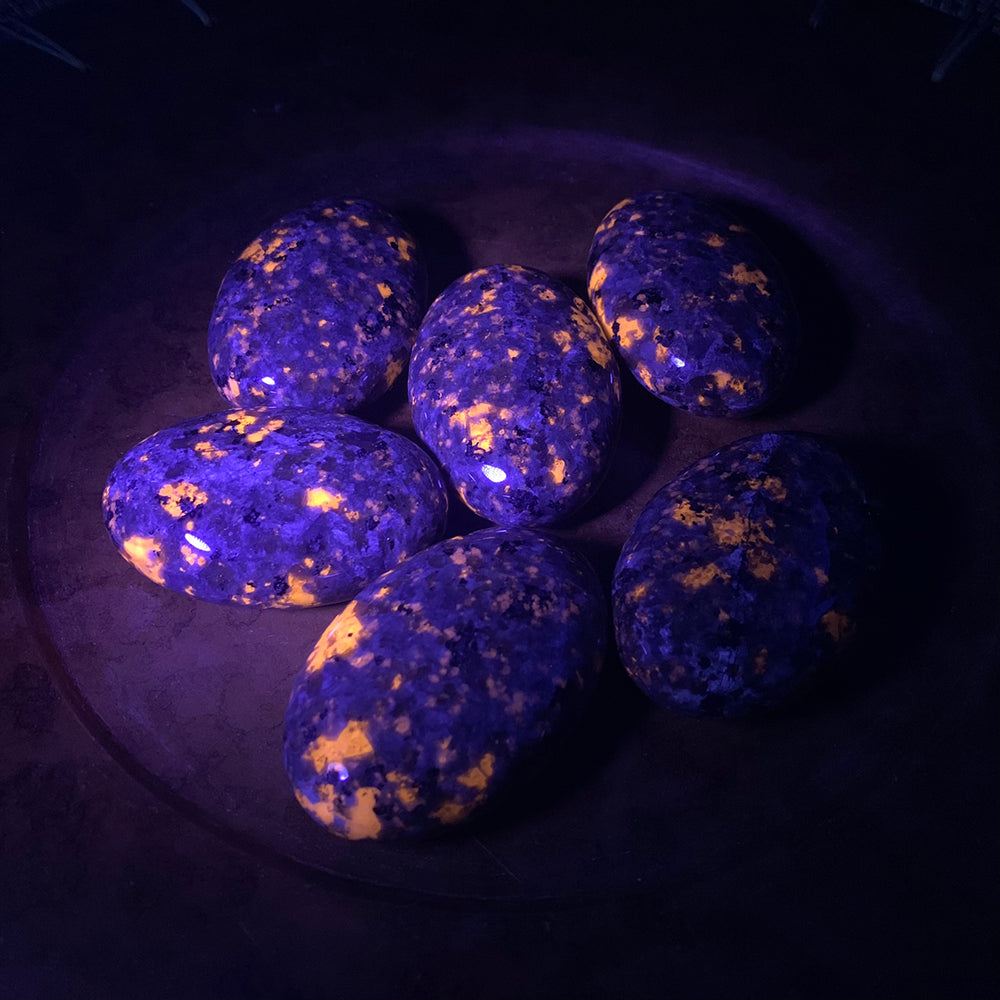 Yooperlite palmstones under UV light in the dark, speckled with glowing orange patches